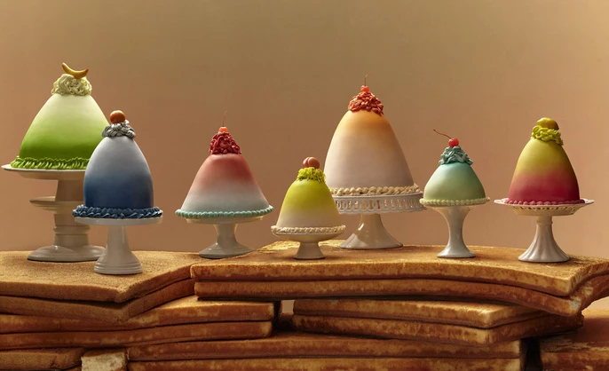 Seven domed cakes of various colors are displayed on pedestals, arranged atop a stack of cake layers, creating a visually striking dessert.