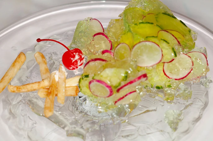 Artistic food presentation featuring french fries, cherry, and radishes on ice, creating a visually striking and unconventional dish.