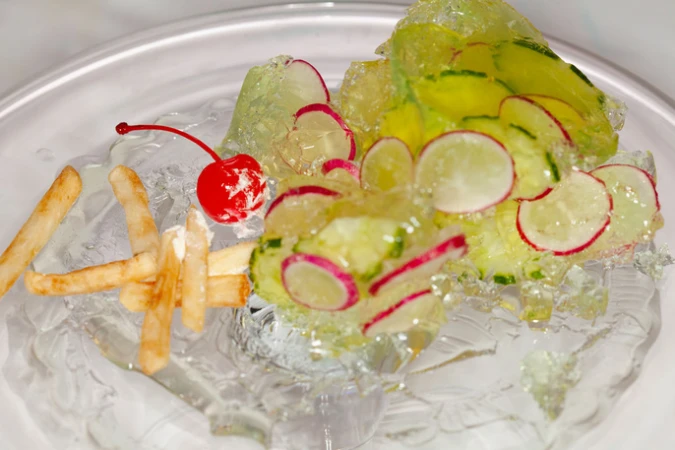 Artistic food presentation featuring french fries, cherry, and radishes on ice, creating a visually striking and unconventional dish.