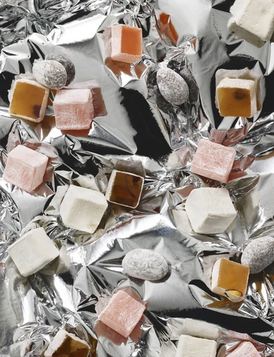 Overhead shot of Turkish delight and sugared almonds scattered on shiny crumpled silver foil, creating a vibrant food still life.