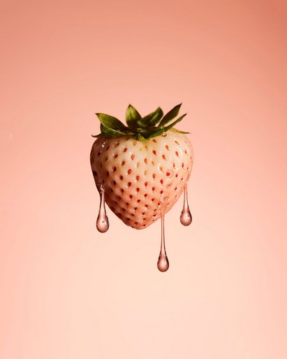 Close-up studio shot of a white strawberry with droplets on a peach-colored background. Food photography of a juicy berry.