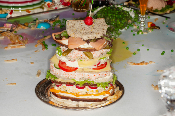 Towering multi-layered sandwich featuring assorted fillings served on silver platter, showcasing culinary creativity and colorful ingredients.