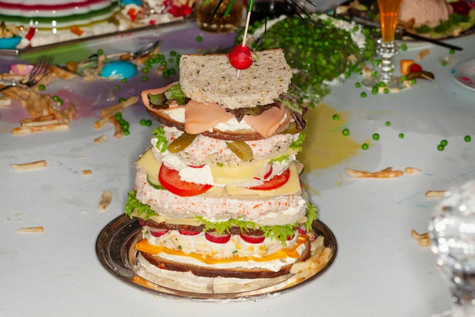 Towering multi-layered sandwich featuring assorted fillings served on silver platter, showcasing culinary creativity and colorful ingredients.