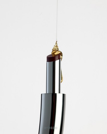 Silver lipstick tube with burgundy lipstick dripping golden liquid against a clean white backdrop in a beauty product shot.