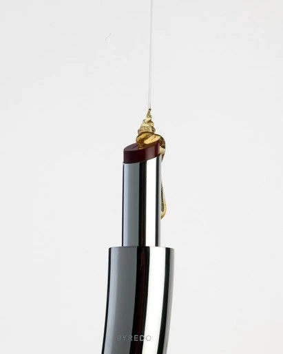 Silver lipstick tube with burgundy lipstick dripping golden liquid against a clean white backdrop in a beauty product shot.