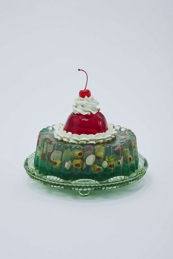 Retro-style gelatin dessert with layers of green and clear Jell-O, filled with fruit, topped with red Jell-O, whipped cream and a cherry.