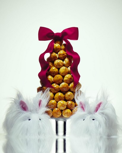 Cone-shaped cake decorated with a ribbon and flanked by white rabbit figures against a white background in a studio setting.