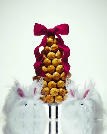 Cone-shaped cake decorated with a ribbon and flanked by white rabbit figures against a white background in a studio setting.