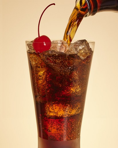Pouring soda into a glass with ice and a cherry, capturing the effervescence and refreshment of the beverage on a neutral background.