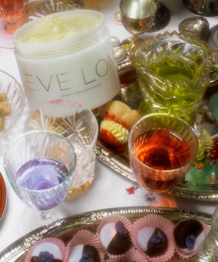 Eve Lom cleanser jar alongside colorful beverages in ornate glassware and miniature desserts arranged on silver serving trays.
