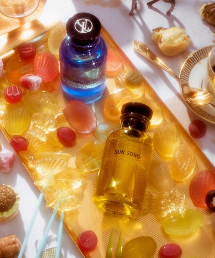 Overhead shot of Louis Vuitton perfume bottles on a gold tray, surrounded by clear and colourful sweets and vintage-style gold spoon and teacup.