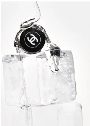 Clear liquid pours over a black designer perfume cap resting on top of stacked ice cubes against a white background