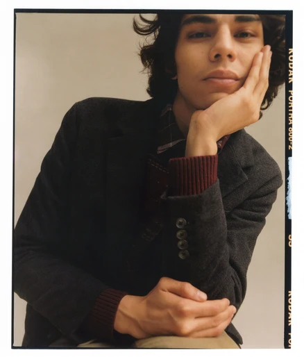 Portrait of a young adult with dark hair wearing a blazer, gazing intently at the camera with a neutral expression in a studio setting.