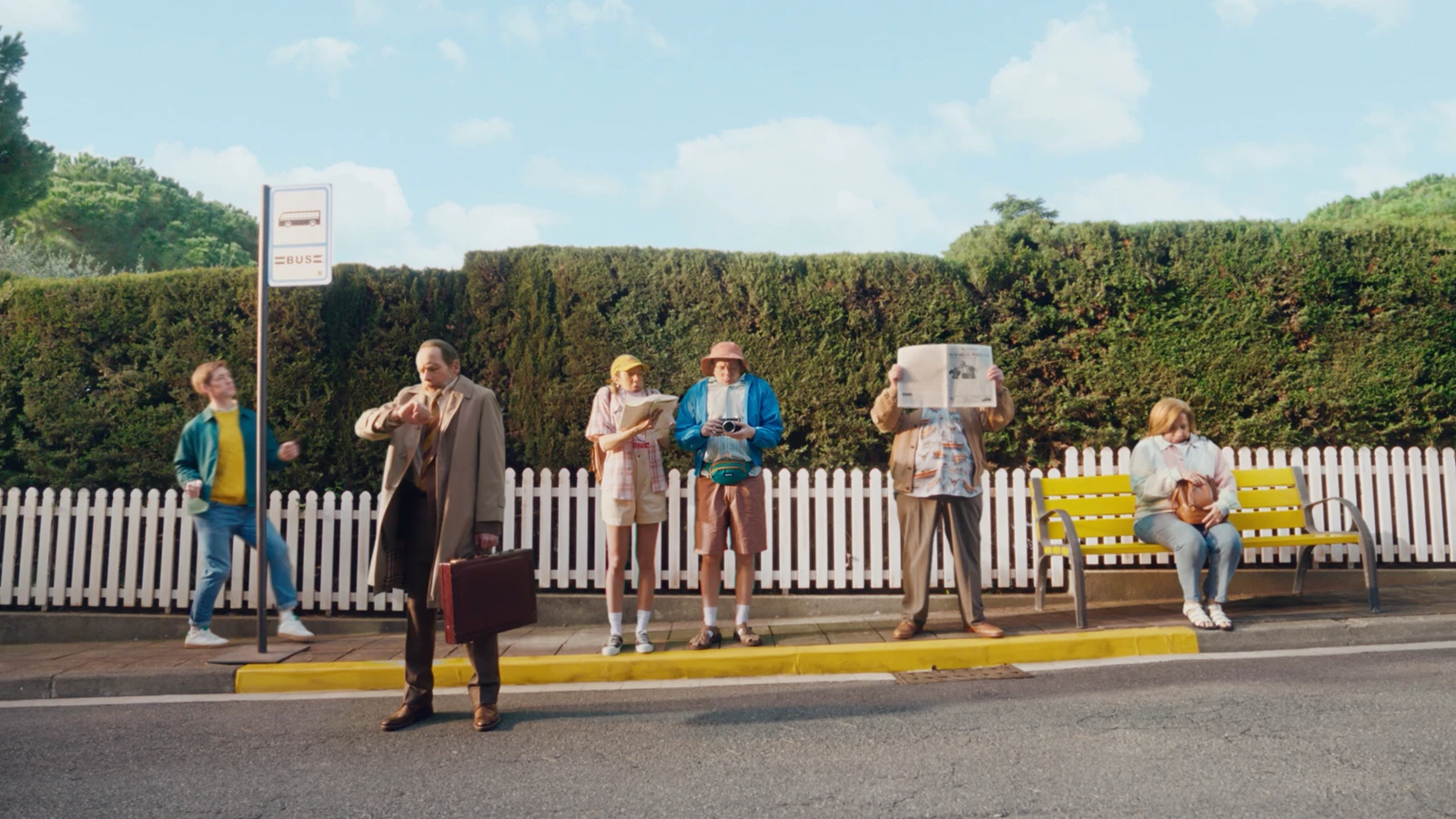 Group of six diverse people waiting at a bus stop along a suburban street directed by Alex Gargot