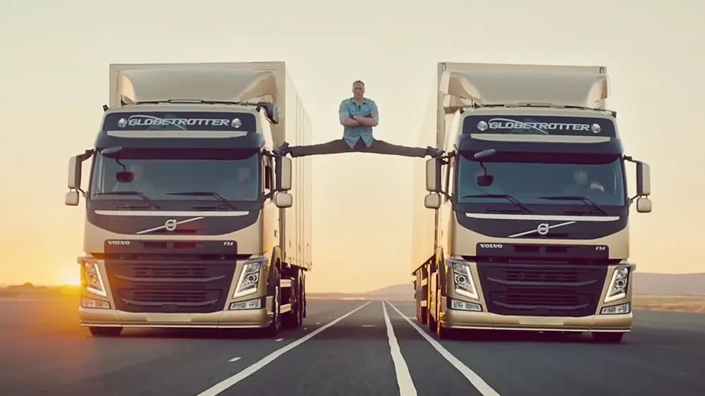 Man does a split between two Volvo trucks on a rural road at sunset, promoting the Volvo brand.