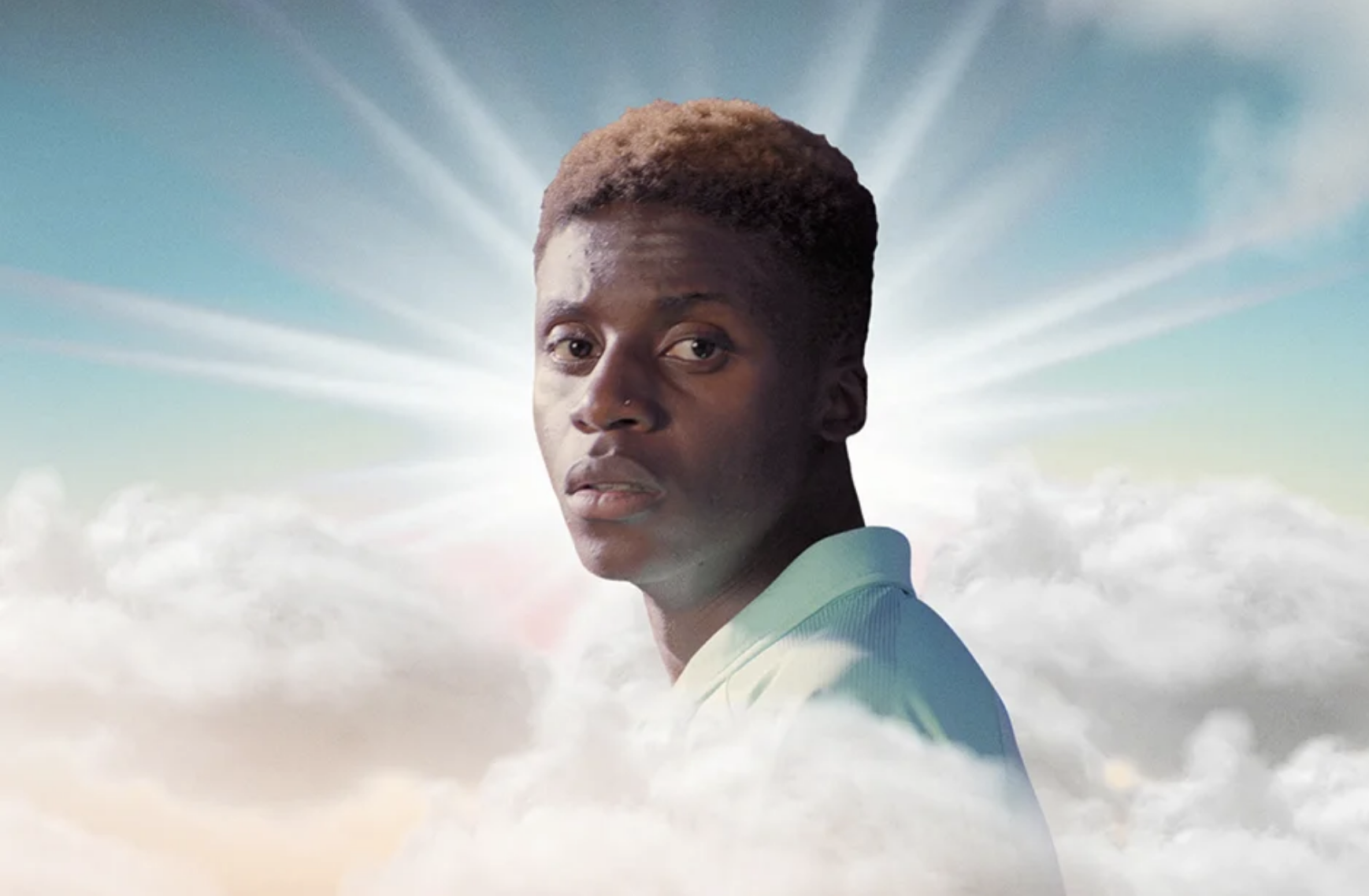 Portrait of a light-skinned Black male model with short hair and wearing a light blue collared shirt, against a sky and cloud background.