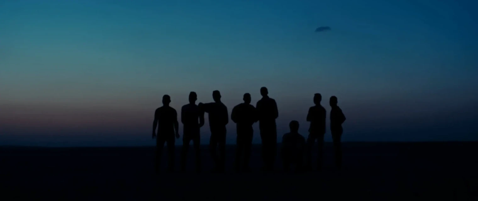 Silhouette of a group of nine people standing in a line outdoors against a twilight sky with blue and dark gradient at dusk.