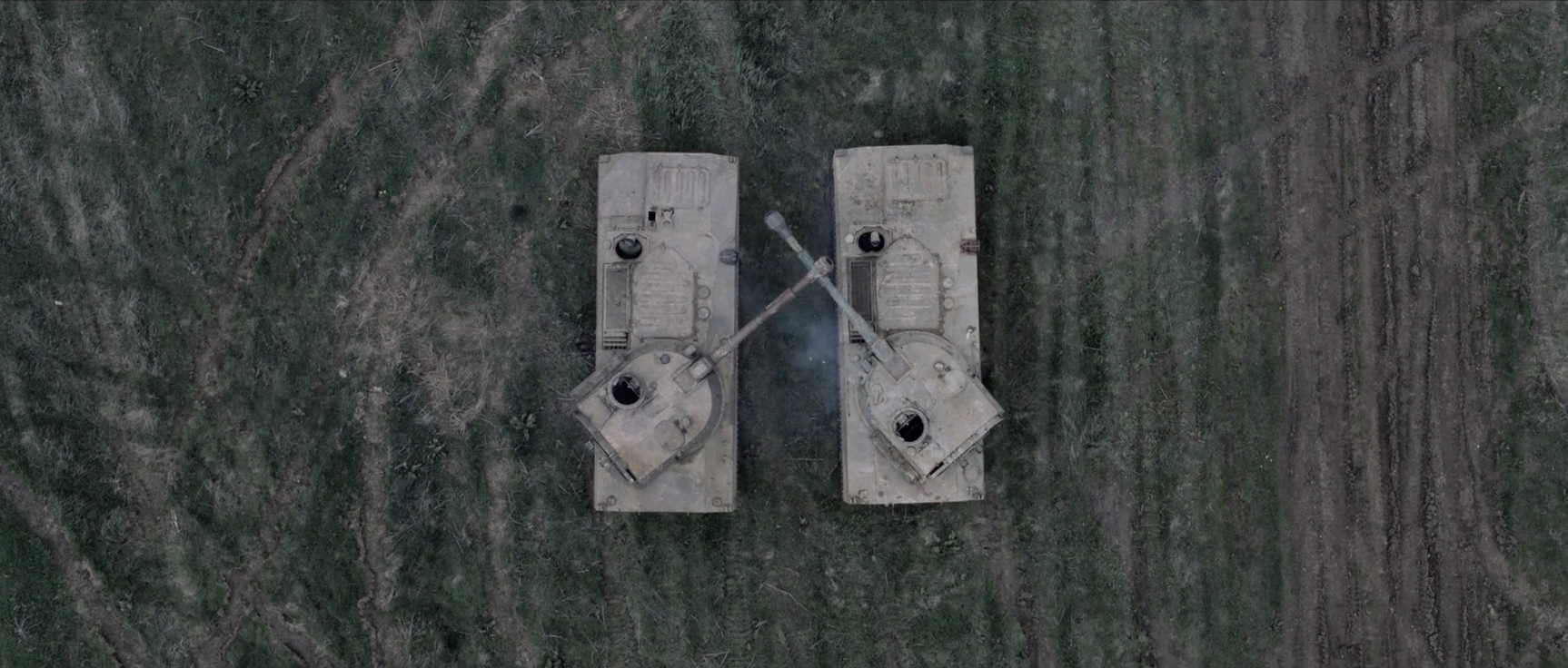 Overhead shot of two tanks facing each other in a field, with smoke visible near their gun turrets, conveying a sense of conflict.