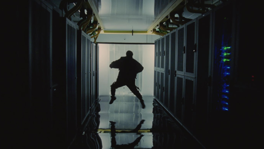 Silhouette of a person jumping mid-air in a dark server room, flanked by rows of server racks with blinking lights.