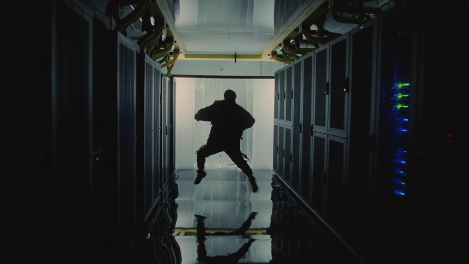 Silhouette of a person jumping mid-air in a dark server room, flanked by rows of server racks with blinking lights.