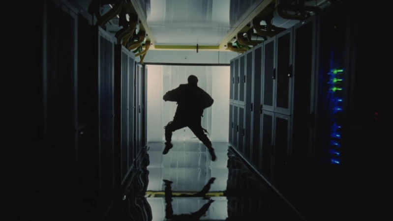 Silhouette of a person jumping mid-air in a dark server room, flanked by rows of server racks with blinking lights.