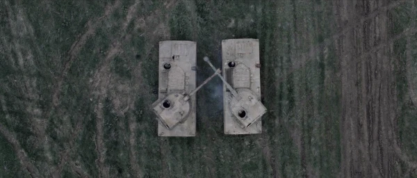 Top-down aerial view of two military tanks facing each other on a dark grassy field with visible tire tracks in Vancouver by Cyprien Clement-delmas