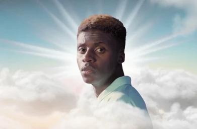 Portrait of a Black man against a sky background with clouds and light rays emanating behind him.