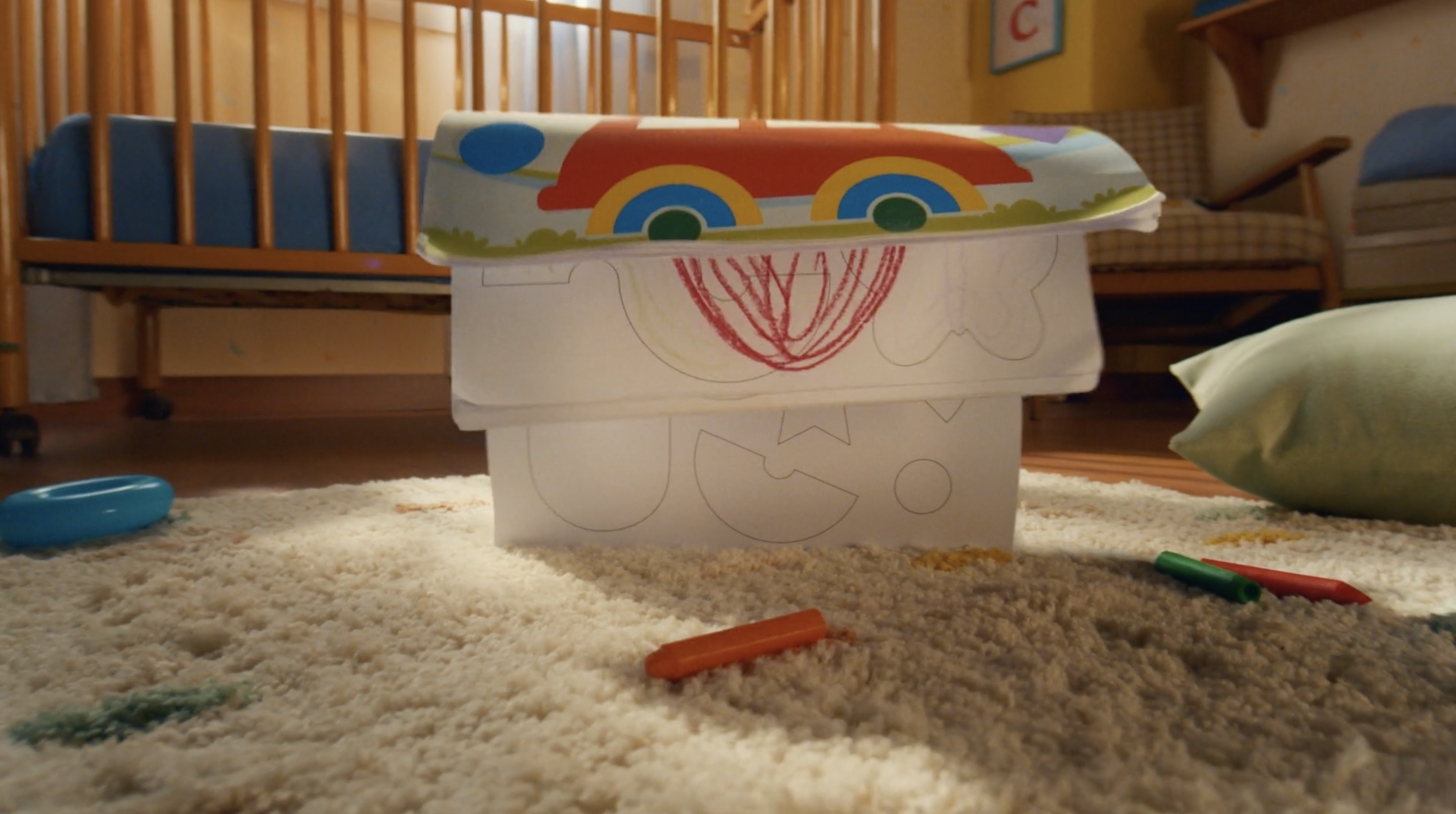 Low-angle view of a children's room with a crib, toy storage boxes decorated with crayon drawings, and colorful crayons on a shag rug.