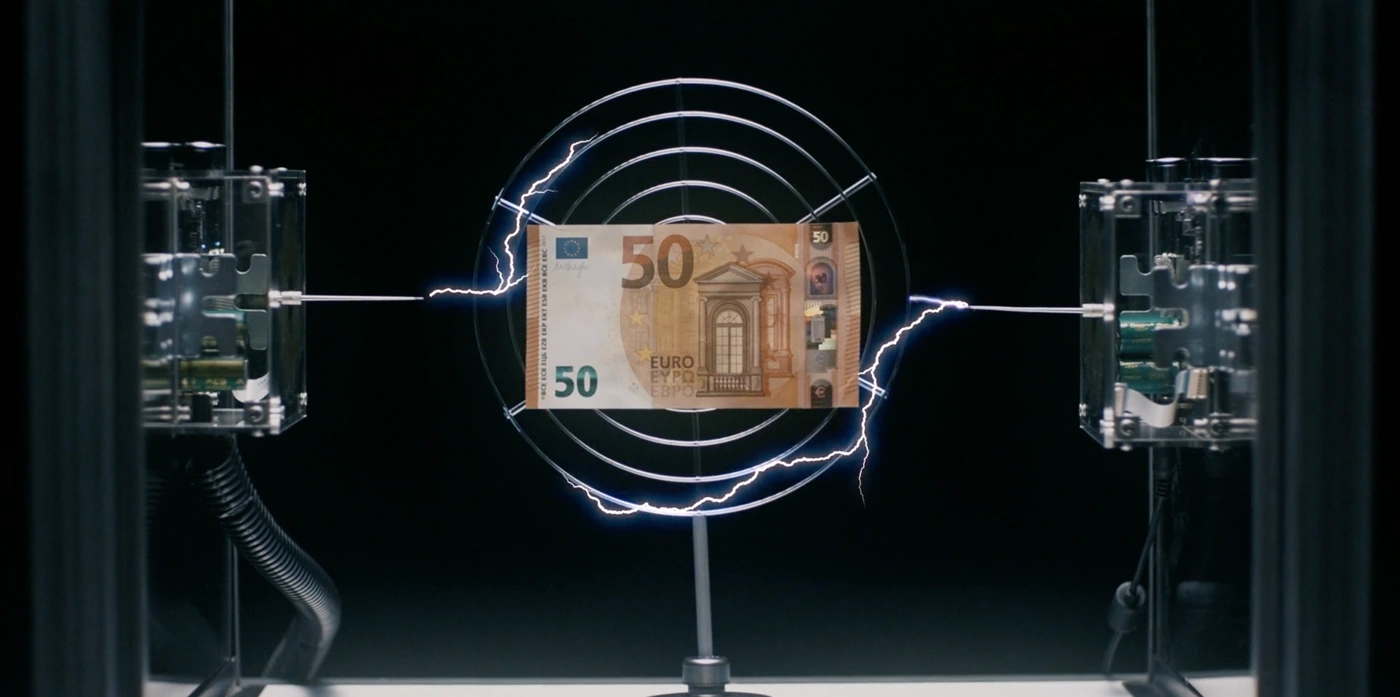 Fifty euro banknote suspended inside a circular metallic apparatus subjected to electric arcs from two side terminals.