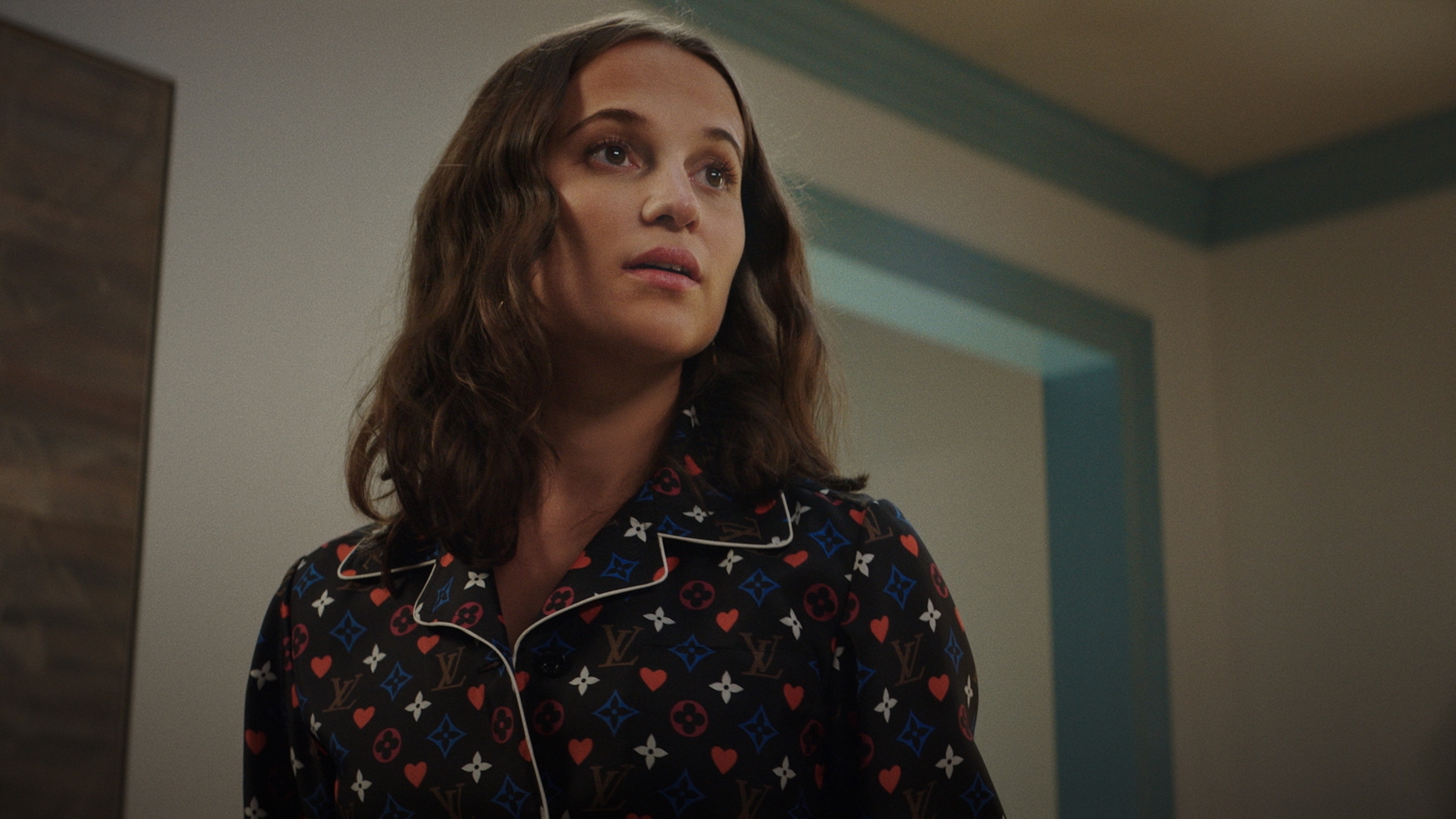Woman in patterned shirt in room. Portrait of a woman with dark hair and fair skin indoors near a doorway with neutral colors.