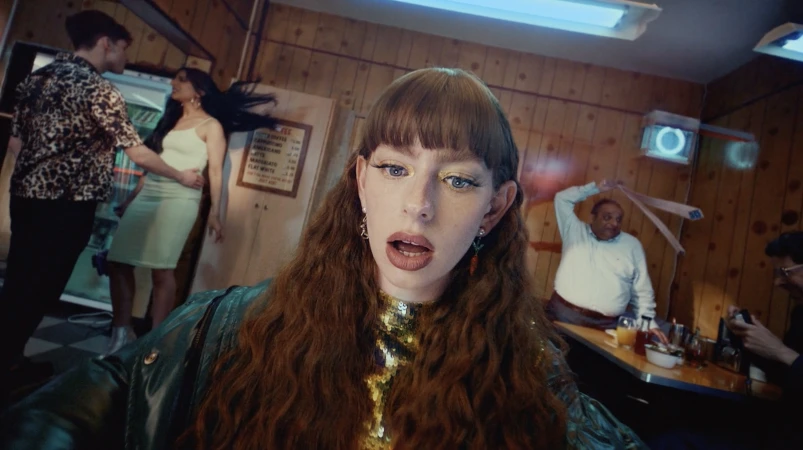 Woman with long wavy auburn hair wearing a sequined top and dark jacket in a diner setting photographed by Lou Escobar.