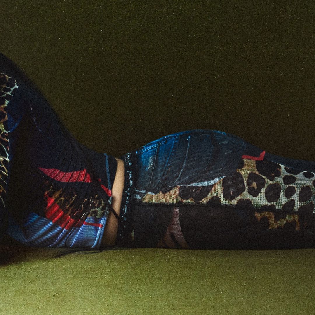 Fashionable woman lying on an olive-green surface wearing patterned clothing. A studio shot with dramatic lighting.