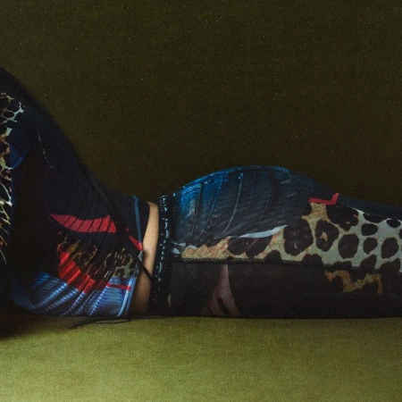Fashionable woman lying on an olive-green surface wearing patterned clothing. A studio shot with dramatic lighting.