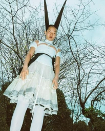 Portrait of an Asian woman in a white layered dress with elaborate pointed black hair standing outdoors against bare trees