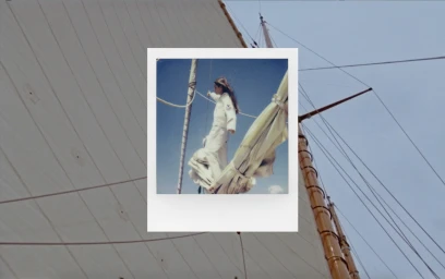 A polaroid style photo showing a woman on a sailboat with rigging against a blue sky, framed by sails.