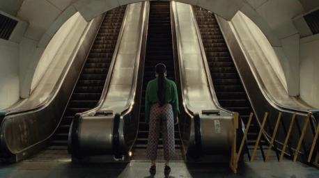 A person seen from behind stands facing ascending escalators in a subway station.