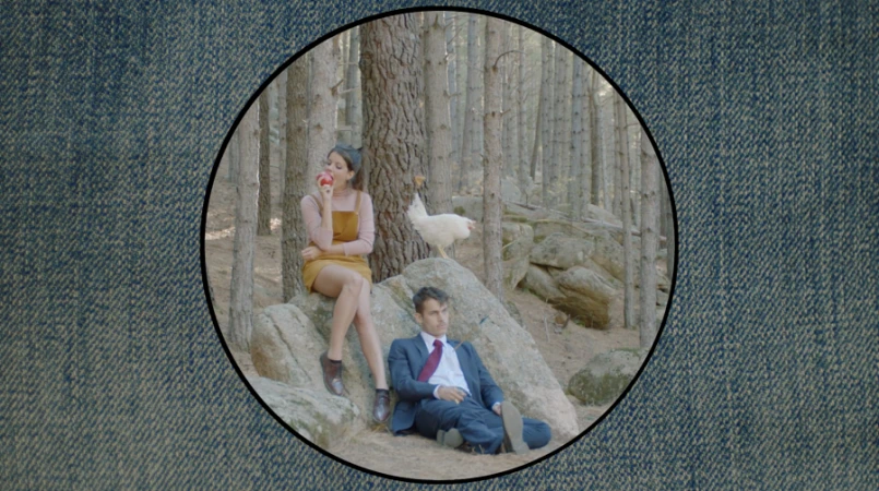Circular frame showing a woman eating an apple on a rock and a man in a suit seated below in a forest with a white chicken.