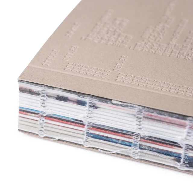Close-up of a hardcover book, showcasing visible layers of pages, binding details, and embossed text on the cover, minimal aesthetic.