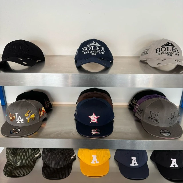 Display of assorted baseball caps on shelves featuring various designs, logos, and colors in an indoor setting, well-lit and organized.