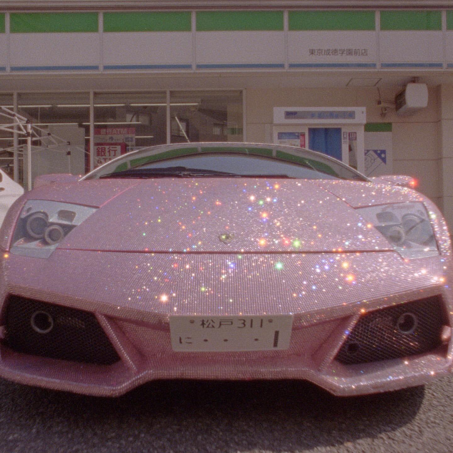 Close-up of a pink, crystal-covered Lamborghini parked in front of a store with a green and white awning, showcasing a blend of luxury and sparkle.