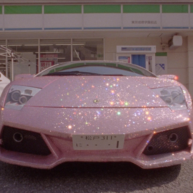 Close-up of a pink, crystal-covered Lamborghini parked in front of a store with a green and white awning, showcasing a blend of luxury and sparkle.