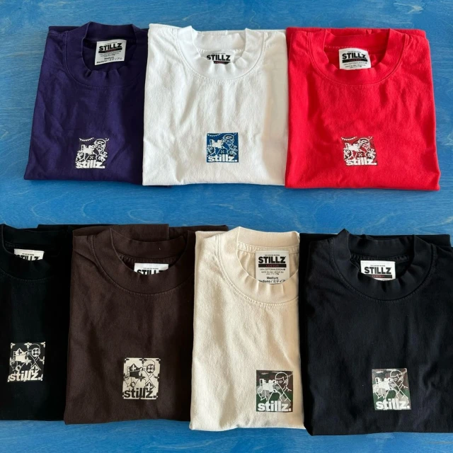 Display of folded t-shirts in various colors, each featuring a small graphic logo, arranged on a blue wooden surface.