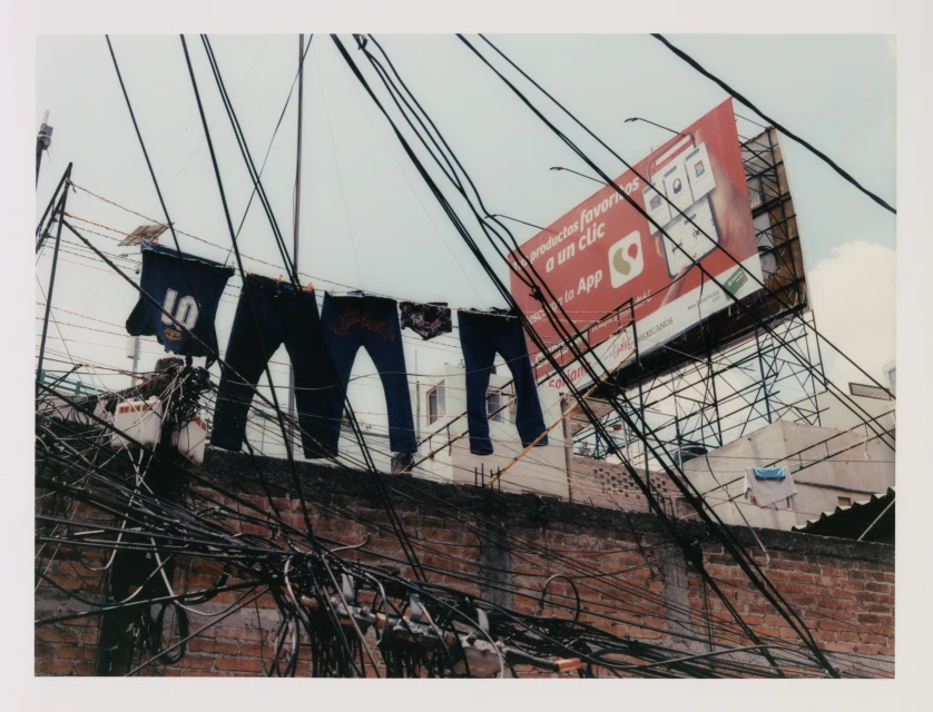 Clothes hanging to dry above a brick building with power lines and a billboard in an outdoor urban environment on a bright day.