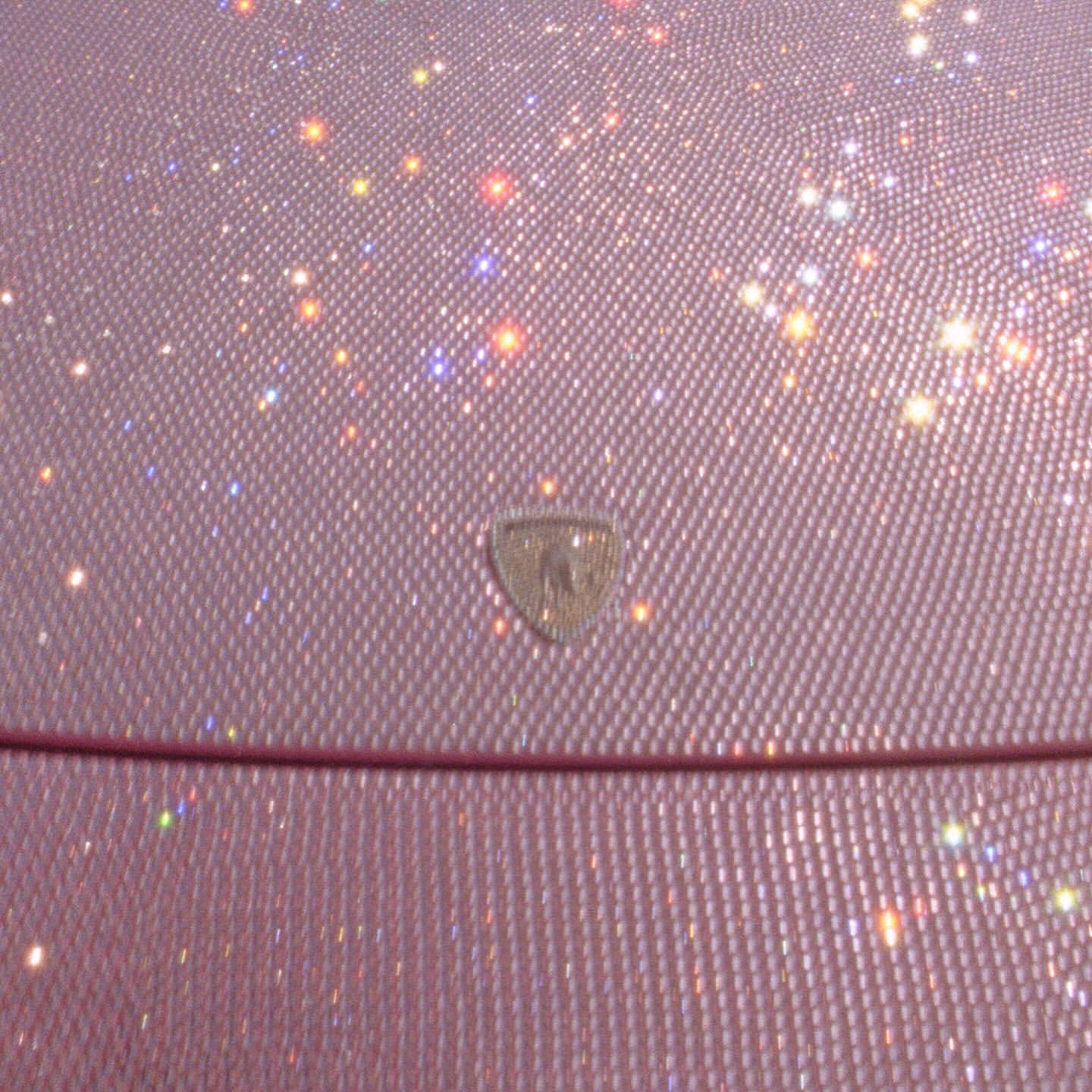 Close-up of a shimmering pink material with a diamond pattern, accented by scattered bokeh lights and a central emblem.