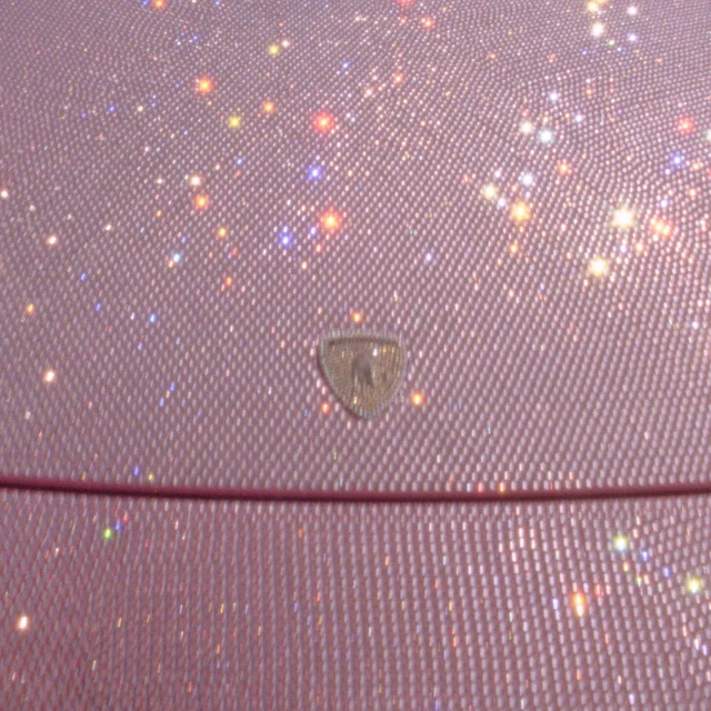 Close-up of a shimmering pink material with a diamond pattern, accented by scattered bokeh lights and a central emblem.