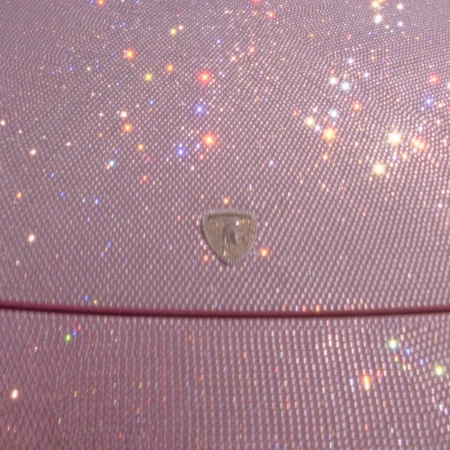 Close-up of a shimmering pink material with a diamond pattern, accented by scattered bokeh lights and a central emblem.