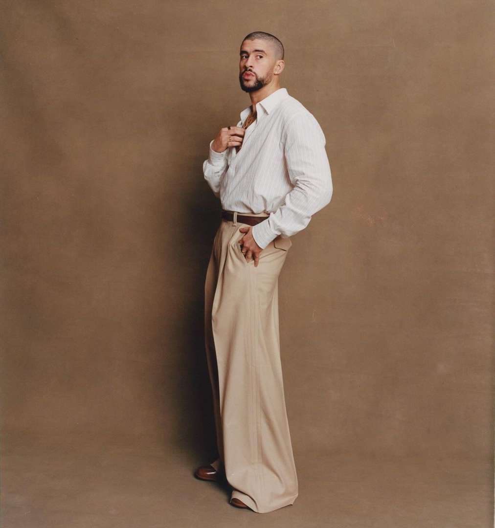 Adult male posing in a studio setting, wearing a striped dress shirt and oversized trousers. The model looks at the camera.