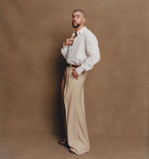 Adult male posing in a studio setting, wearing a striped dress shirt and oversized trousers. The model looks at the camera. 