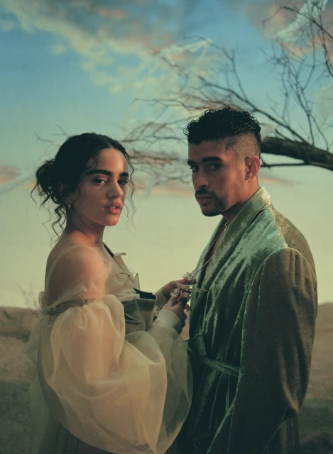 A stylish portrait featuring a fashionable couple; a woman in a flowing gown and a man in a robe, set against a muted background.