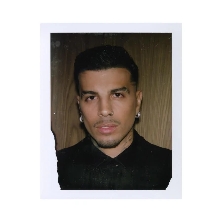 Polaroid photograph of a man in a black shirt against a wood panel background by Stillz